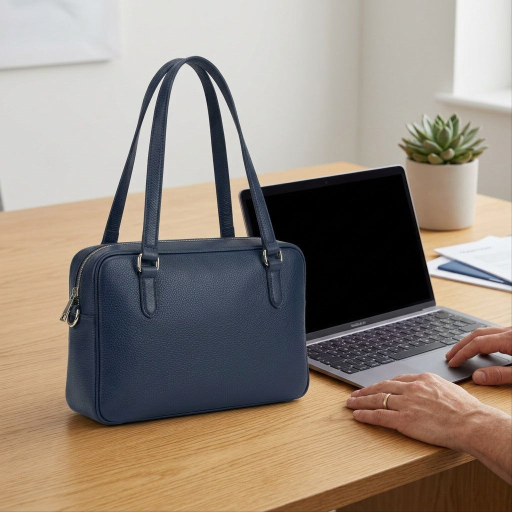 The leather tote bag is shown relative to a human hand for size comparison.