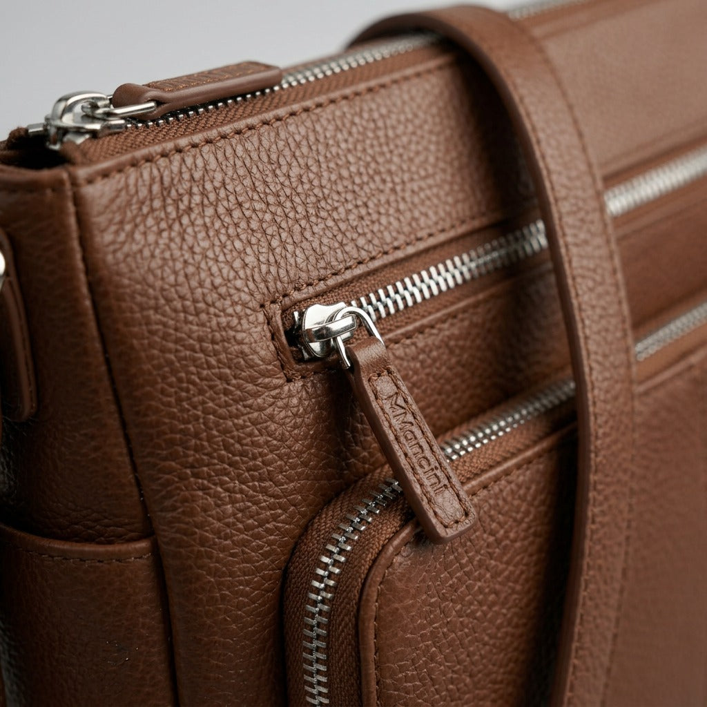 Macro of brown pebbled leather texture and precision Mancini logo embossed metal zipper pull.