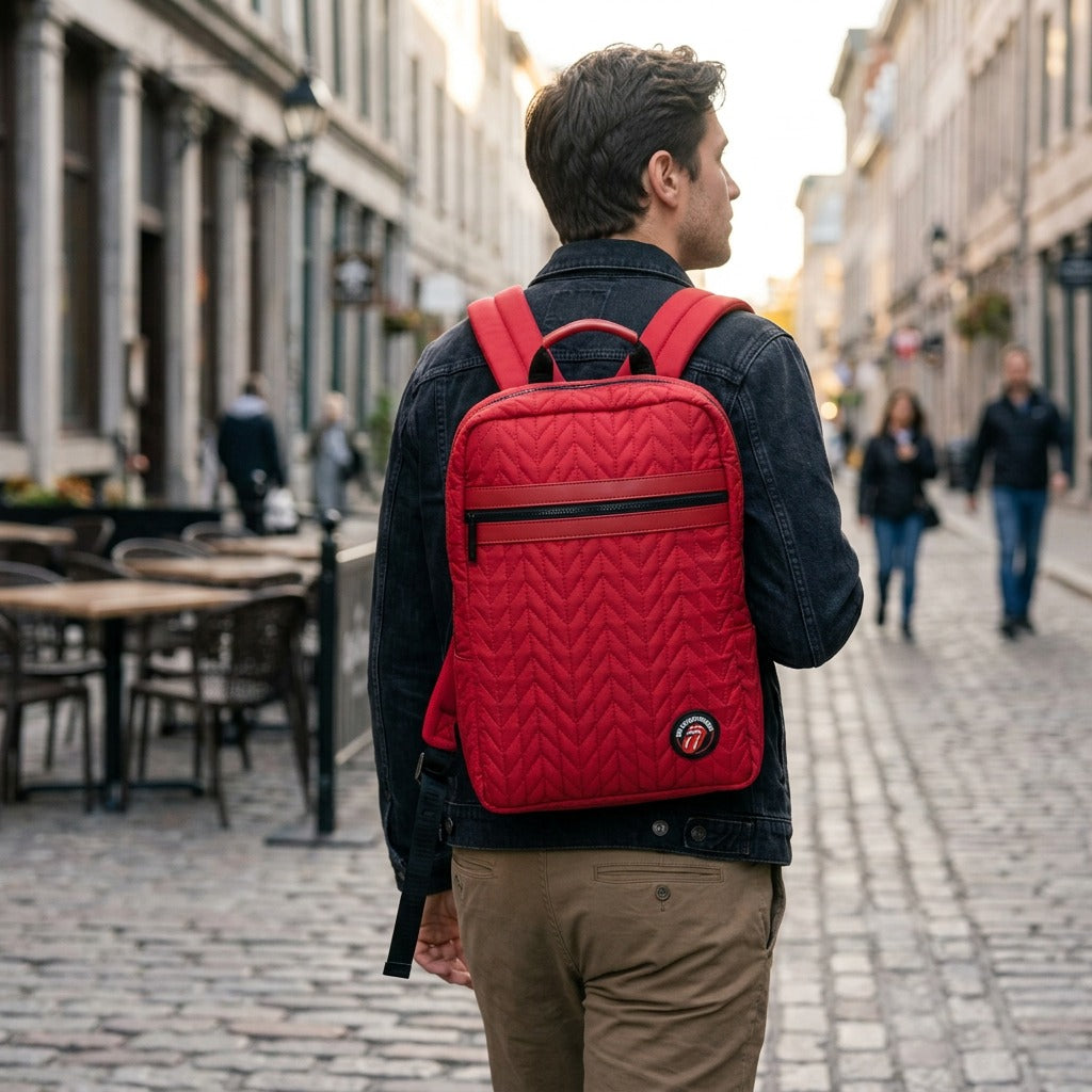 A lifestyle image featuring the red quilted Rolling Stones backpack worn by a person walking through an urban setting.
